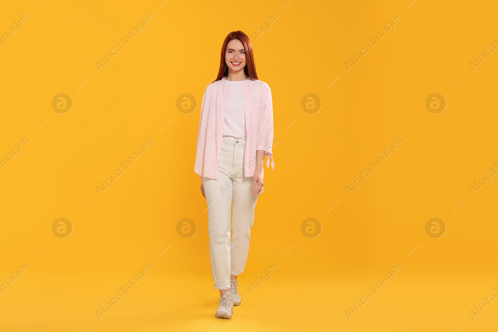 Photo of Happy woman with red dyed hair walking on orange background