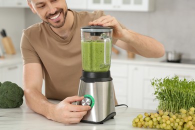 Photo of Happy man blending delicious smoothie at white marble table in kitchen, closeup