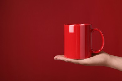 Photo of Woman holding porcelain mug on red background, closeup. Space for text