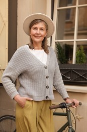 Beautiful senior woman standing near bicycle outdoors