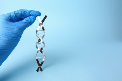 Scientist with DNA molecular chain model made of metal on light blue background, closeup. Space for text