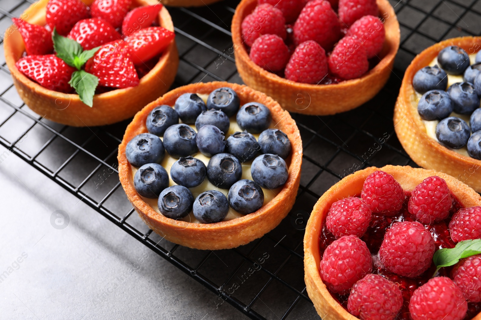 Photo of Tartlets with different fresh berries on grey table. Delicious dessert