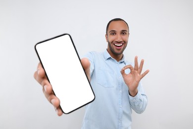 Young man showing smartphone in hand and OK gesture on white background