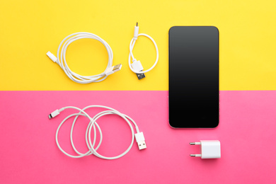 Photo of USB charge cables, power adapter and smartphone on color background, flat lay. Modern technology