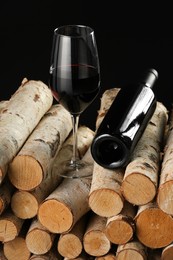 Photo of Red wine in wineglass and bottle on wooden logs against black background