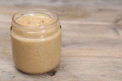 Tasty nut paste in jar on wooden table, closeup. Space for text