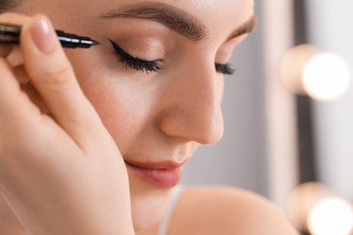 Makeup product. Woman applying black eyeliner indoors, closeup