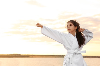 Photo of Cute little girl in kimono practicing karate near river at sunset