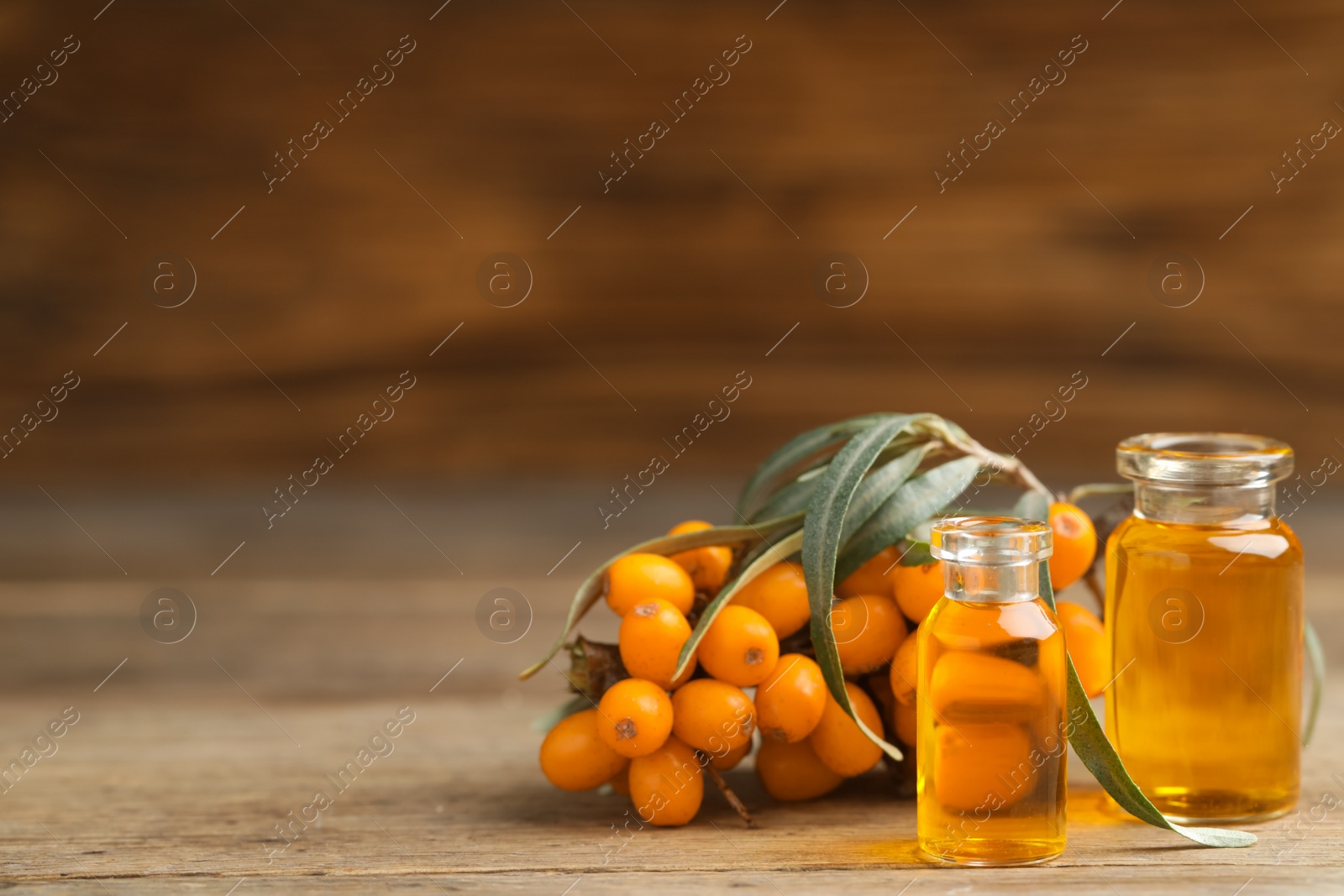 Photo of Natural sea buckthorn oil and fresh berries on wooden table. Space for text
