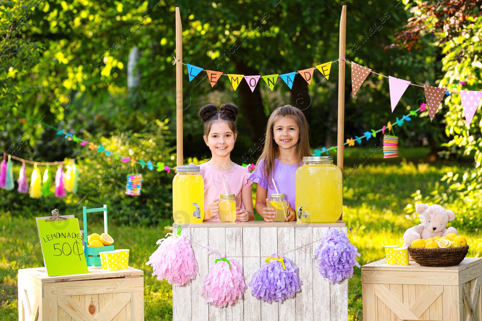 Photo of Cute little girls at lemonade stand in park. Summer refreshing natural drink