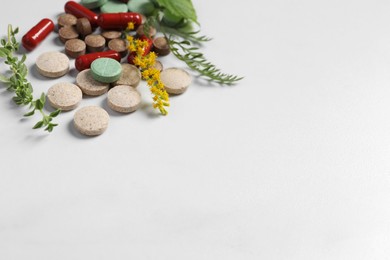 Different pills and herbs on white table, space for text. Dietary supplements