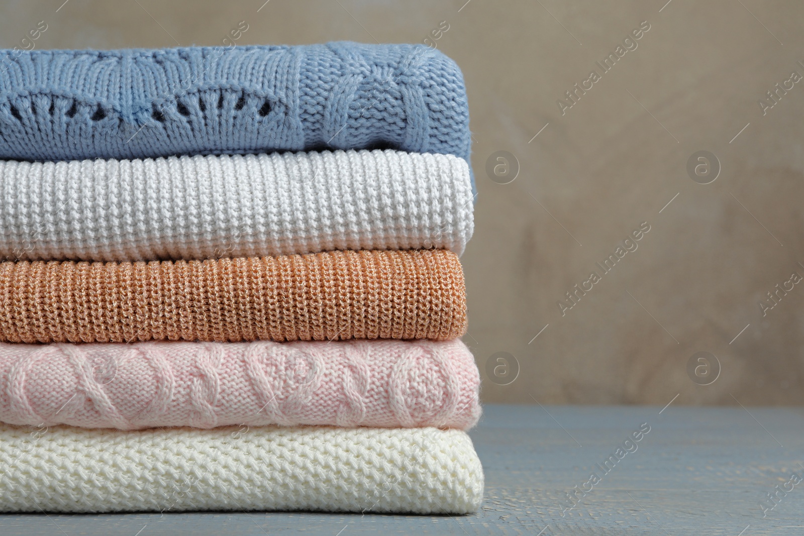 Photo of Stack of warm clothes on wooden table against grey background. Autumn season