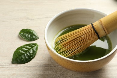 Photo of Cup of fresh matcha tea with bamboo whisk and leaves on white wooden table, closeup