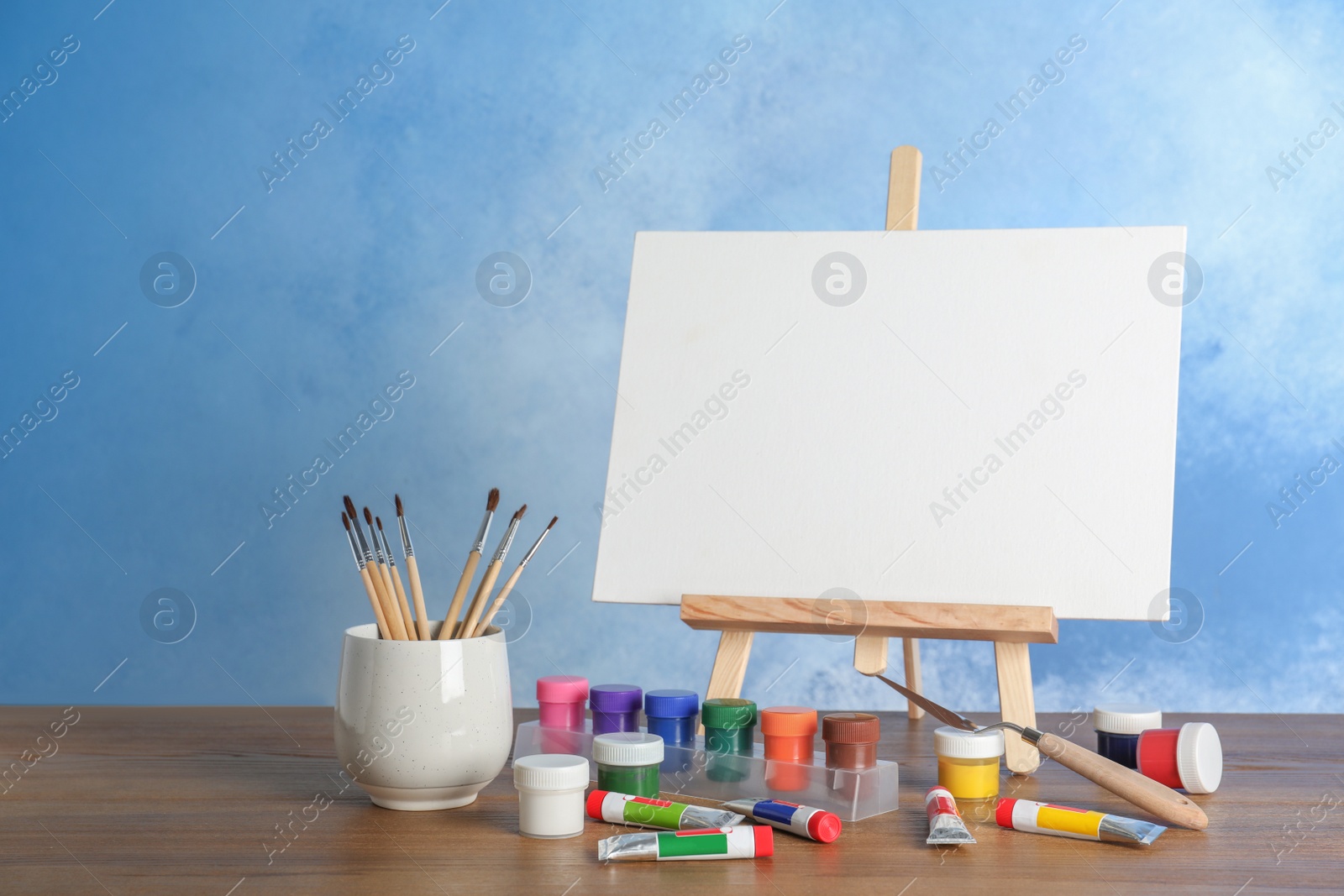 Photo of Wooden easel with blank canvas board and painting tools for children on table near color wall. Space for text