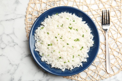 Photo of Mat with plate of boiled rice and fork on marble background, top view