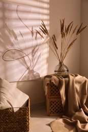 Vase with decorative dried plants and painting in stylish room interior