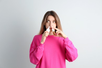 Photo of Sick young woman using nasal sprays on white background