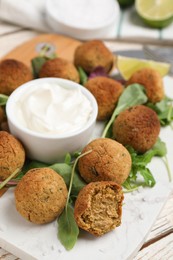 Photo of Delicious falafel balls with herbs and sauce on white table, closeup