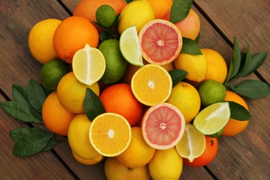 Photo of Different citrus fruits with green leaves on wooden table, flat lay