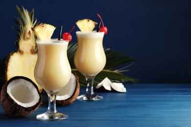 Photo of Tasty Pina Colada cocktails and ingredients on blue wooden table, space for text