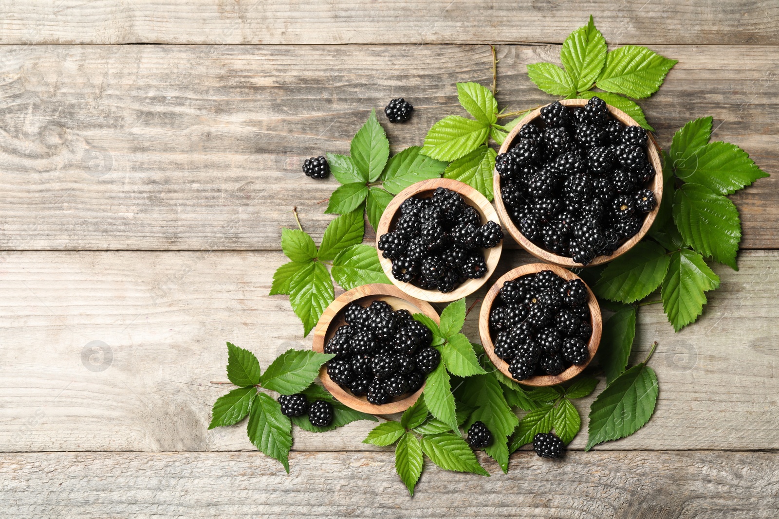 Photo of Ripe blackberries and green leaves on wooden table, flat lay. Space for text