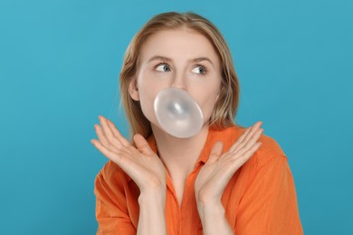 Photo of Beautiful young woman blowing bubble gum on light blue background