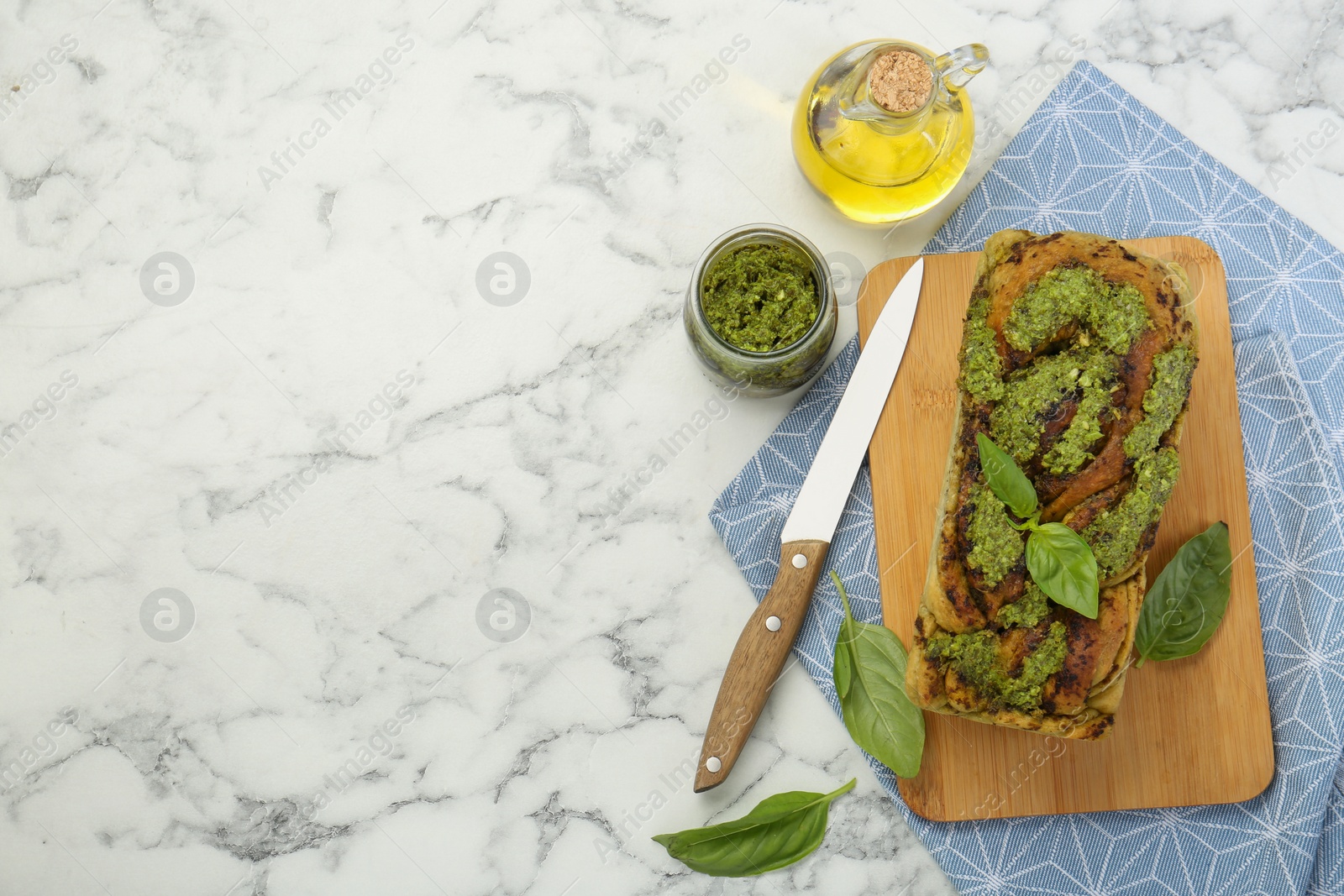 Photo of Freshly baked pesto bread with basil and knife on white marble table, flat lay. Space for text