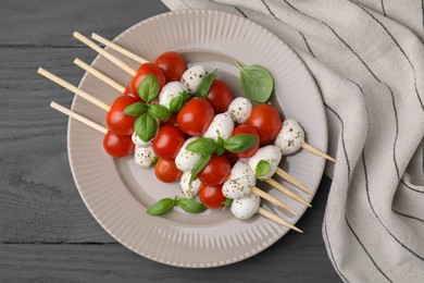 Photo of Caprese skewers with tomatoes, mozzarella balls, basil and spices on grey wooden table, top view
