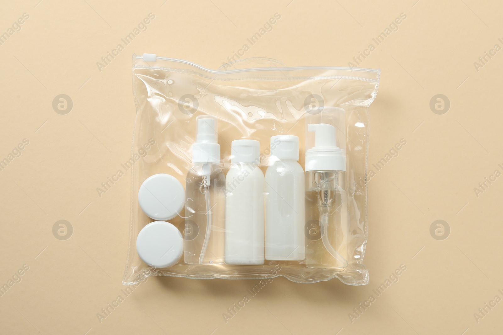 Photo of Cosmetic travel kit in plastic bag on beige background, top view. Bath accessories