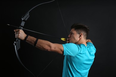 Photo of Man with bow and arrow practicing archery on black background