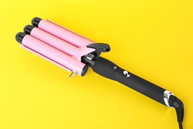 Photo of Modern triple curling iron on yellow background