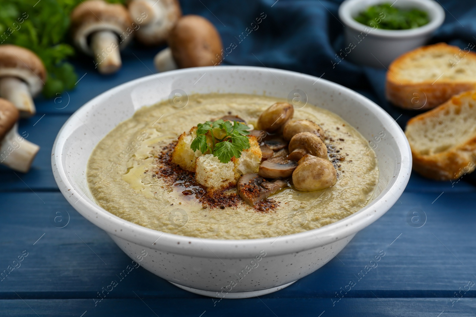 Photo of Delicious cream soup with mushrooms and croutons on blue wooden table