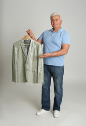 Photo of Senior man holding hanger with jacket in plastic bag on light grey background. Dry-cleaning service