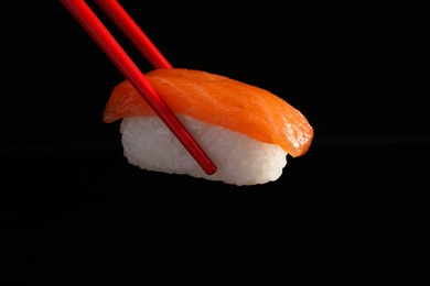 Photo of Chopsticks with delicious nigiri sushi on black background, closeup