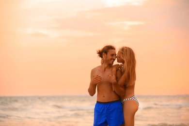 Photo of Young woman in bikini and her boyfriend on beach at sunset. Lovely couple