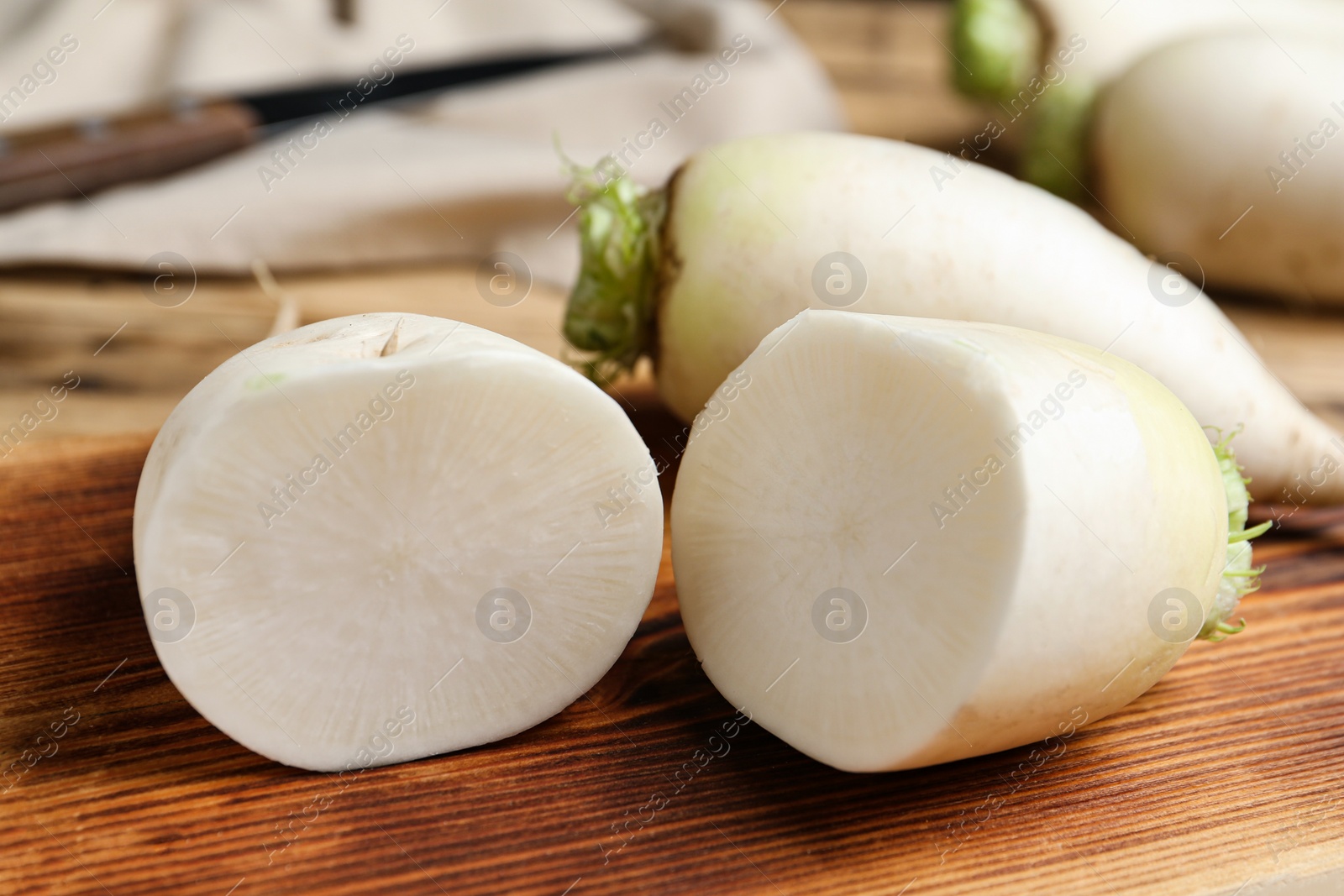 Photo of Cut and whole white turnips on wooden board, closeup