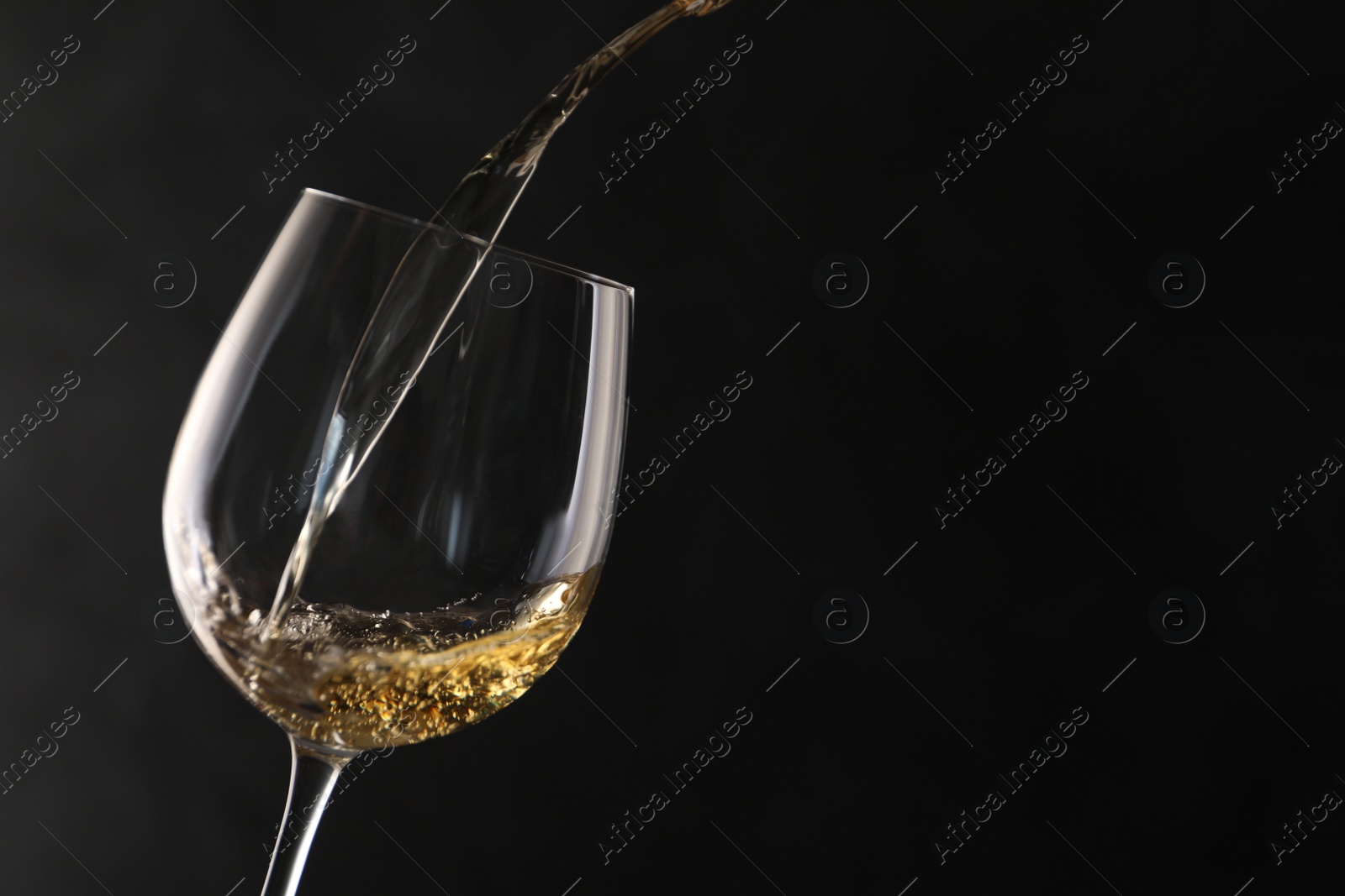 Photo of Pouring white wine into glass on dark background. Space for text