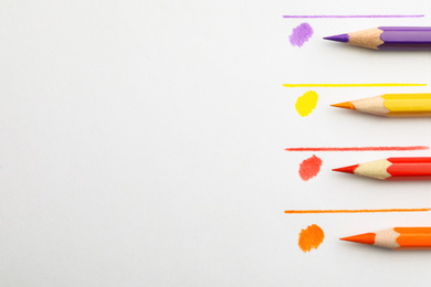 Colorful pencils with swatches on white background, top view