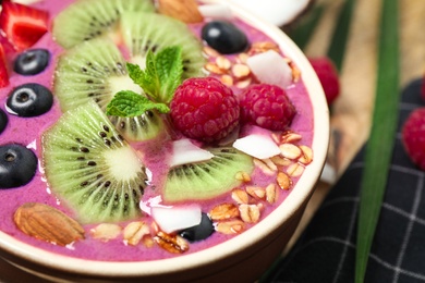 Delicious acai smoothie with granola and fruits in dessert bowl, closeup