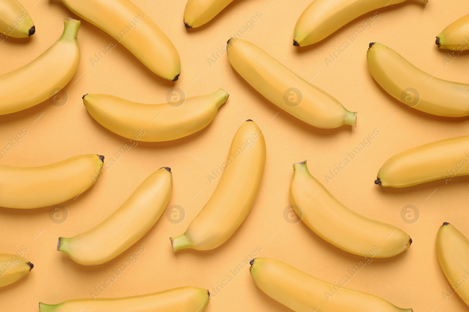 Photo of Sweet ripe baby bananas on light orange background, flat lay