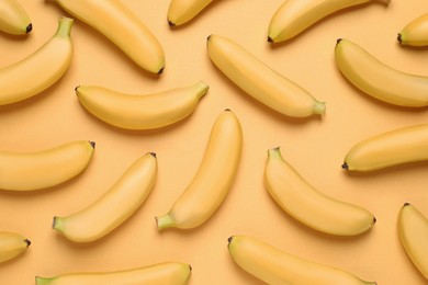 Photo of Sweet ripe baby bananas on light orange background, flat lay