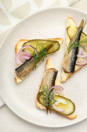 Photo of Delicious sandwiches with sprats, pickled cucumber, onion and dill served on white wooden table, top view