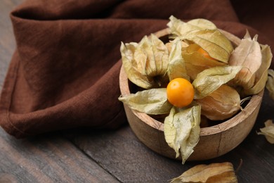 Ripe physalis fruits with calyxes in bowl on wooden table, space for text