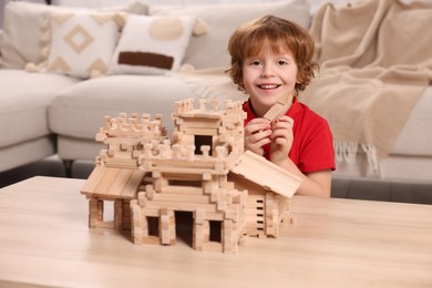 Photo of Cute little boy playing with wooden castle at table in room. Child's toy