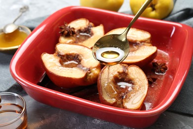 Photo of Pouring tasty honey onto baked quinces in dish on grey textured table, closeup