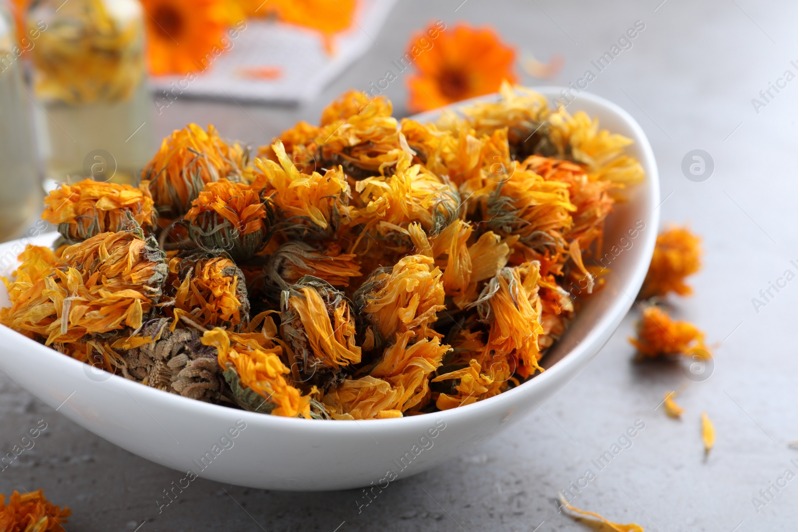 Photo of Plate of dry calendula flowers on grey table, closeup