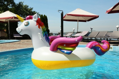 Photo of Funny inflatable unicorn ring floating in swimming pool on sunny day, outdoors