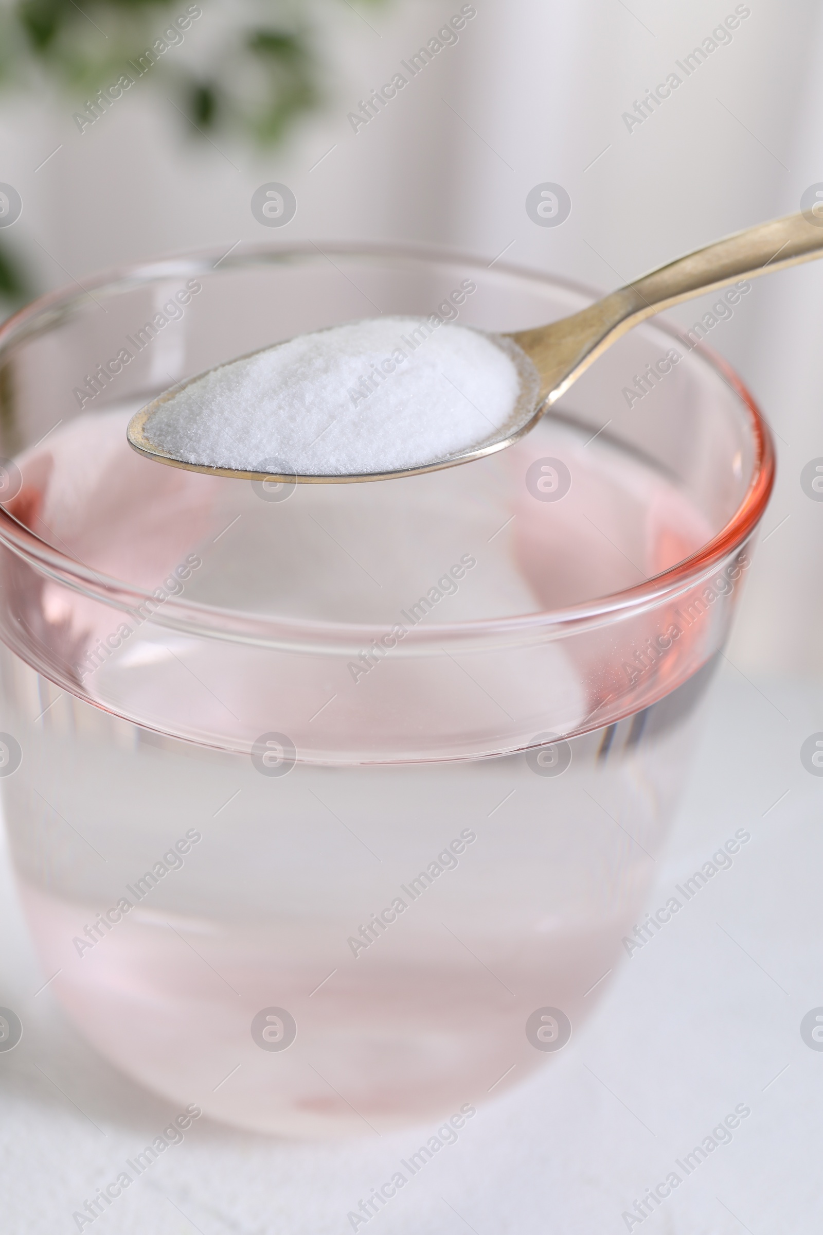 Photo of Spoon with baking soda over glass of water on white table, closeup