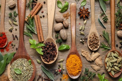 Photo of Different herbs and spices with spoons on wooden table, flat lay
