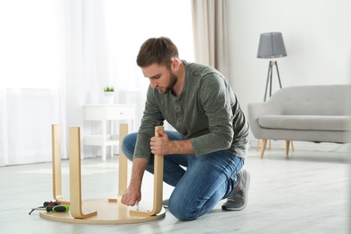 Photo of Young working man repairing table at home